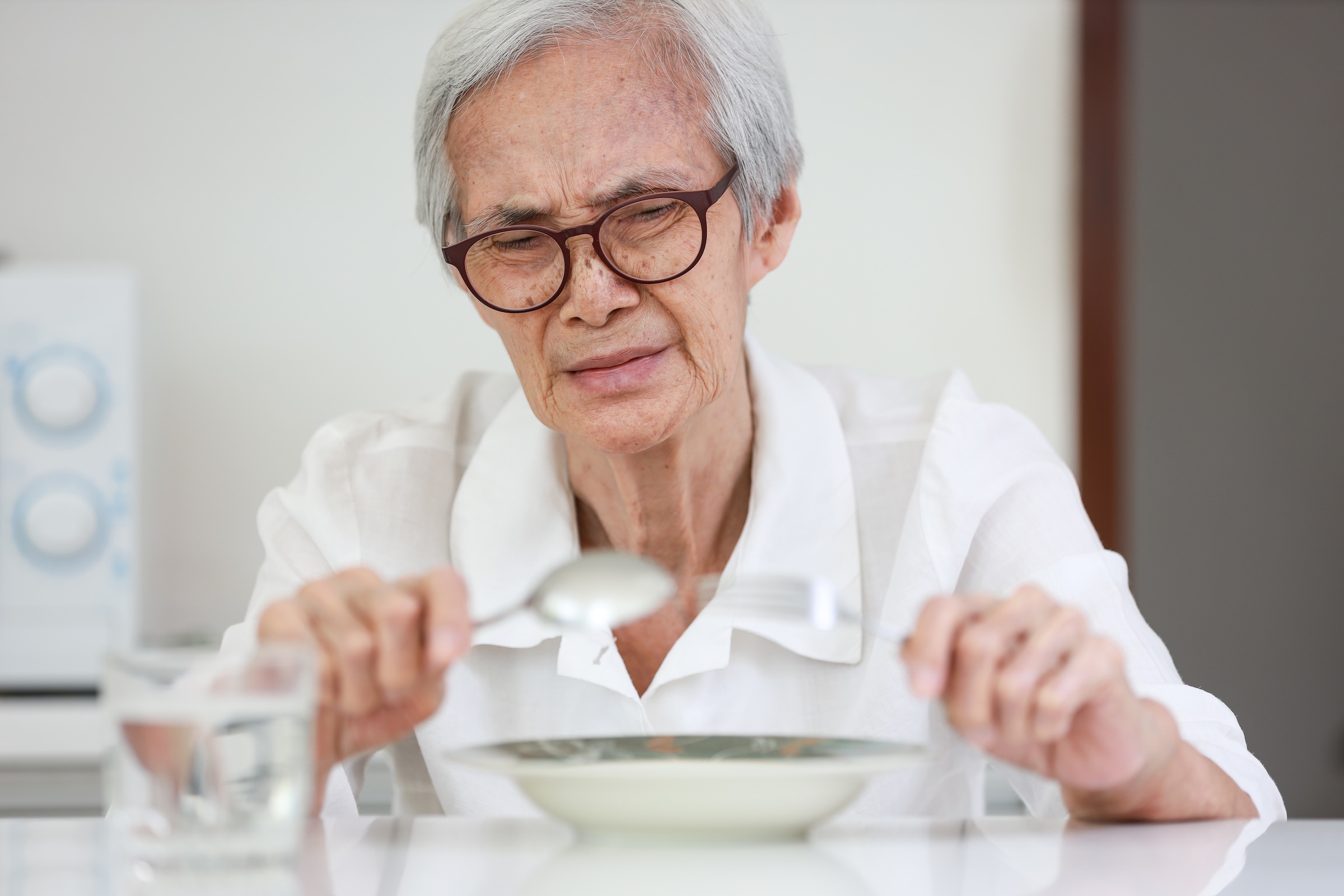 Seniorka patrzy na jedzenie, ale nie ma apetytu i wykrzywia twarz